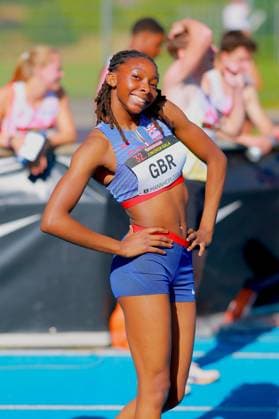 An athlete from Great Britain poses smiling on the tartan track of the Michael Hoffmann Stadium in Mannheim Her bib number reads GBR and the words 32 Junior Gala Mannheim 2024 Athlete from Great Britain at the 32 Junior Gala in Mannheim Copyright: xspeedshotx