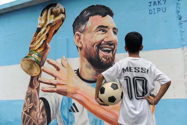 June 14, 2026: Sylhet, Bangladesh: A child wearing a jersey bearing the name and number of Argentine football player Lionel Messi looks toward a mural of Messi while holding a football. World Cup 2026: Argentine Football Fever Grips Bangladesh  - ZUMAr143 20260614_zap_r143_003 Copyright: xMdxRafayatxHaquexKhanx