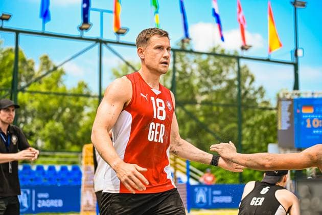Robin John ( 18; Deutschland Beachhandball Nationalmannschaft) klatscht mit einem Mitspieler ab, Sand spritzt von den Händen. Im Hintergrund sind Länderflaggen und die Anzeigetafel am Jarun See in Zagreb zu sehen. IHF Beach Handball World Championship, WM, Weltmeisterschaft 2026, 23.06.2026, Zagreb, Jarun See *** Robin John 18, a member of the German national beach handball team, high-fives a teammate; sand sprays from their hands. In the background, national flags and the scoreboard at Lake Jarun in Zagreb can be seen. IHF Beach Handball World Championship 2026, June 23, 2026, Zagreb, Lake Jarun,detected_source_language Copyright: xspeedshotx xDorianfrickx