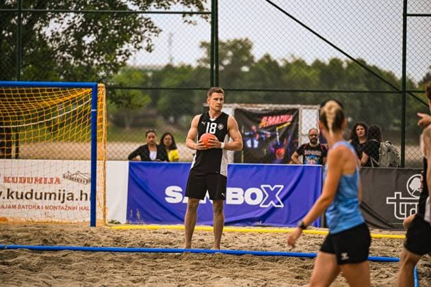 Robin John ( 18; Deutsche Beachhandball Nationalmannschaft) steht mit dem Ball in den Händen auf dem Sandfeld und bereitet eine Aktion vor. Im Vordergrund ist eine Gegenspielerin der USA zu sehen, im Hintergrund das gelbe Tor und Zuschauer. IHF Beach Handball World Championship, WM, Weltmeisterschaft 2026, 23.06.2026, Zagreb, Jarun See *** Robin John 18 Copyright: xspeedshotx xDorianfrickx