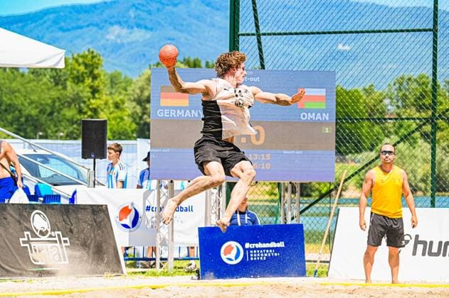 Ein Spieler der deutschen Beachhandball-Nationalmannschaft springt im Shoot-out hoch und holt zum Wurf aus, der Ball ist klar in der erhobenen Hand sichtbar. Im Hintergrund zeigt die Anzeigetafel das Duell Germany vs. Oman beim Turnier am Jarun See in Zagreb. IHF Beach Handball World Championship, WM, Weltmeisterschaft 2026, 23.06.2026, Zagreb, Jarun See *** A player on the German national beach handball team jumps high during a shootout and winds up to shoot; the ball is clearly visible in his raised hand. In the background, the scoreboard displays the Germany vs. Oman match at the 2026 IHF Beach Handball World Championship tournament at Lake Jarun in Zagreb, June 23, 2026, Zagreb, Lake Jarun Copyright: xspeedshotx xDorianfrickx