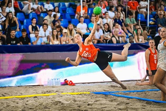 Eine Spielerin im orangefarbenen Trikot führt einen akrobatischen Drehwurf aus und hält den grünen Ball in ausgestreckter Hand, während sie durch den Sand fliegt. Im Hintergrund verfolgen zahlreiche Zuschauer auf blauen Tribünen die Szene. IHF Beach Handball World Championship, WM, Weltmeisterschaft 2026, 23.06.2026, Zagreb, Jarun See *** A player in an orange jersey performs an acrobatic spin shot and holds the green ball in her outstretched hand as she flies through the sand. In the background, numerous spectators in the blue stands watch the scene. 2026 IHF Beach Handball World Championship, June 23, 2026, Zagreb, Lake Jarun Copyright: xspeedshotx xDorianfrickx