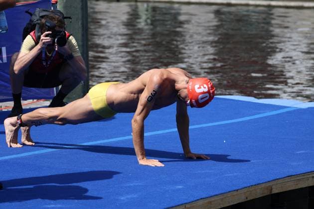 Ein Triathlet verlässt das Wasser und dehnt sich auf der blauen Ausstiegsmatte aus. Im Hintergrund dokumentiert ein Fotograf die Szene an der Binnenalster. Triathlet nach dem Schwimmen an der Binnenalster Hamburg *** A triathlete exits the water and stretches out on the blue exit mat. In the background, a photographer captures the scene at the Binnenalster: a triathlete after the swim at the Binnenalster in Hamburg. Copyright: xspeedshotx xSarahxWolfx