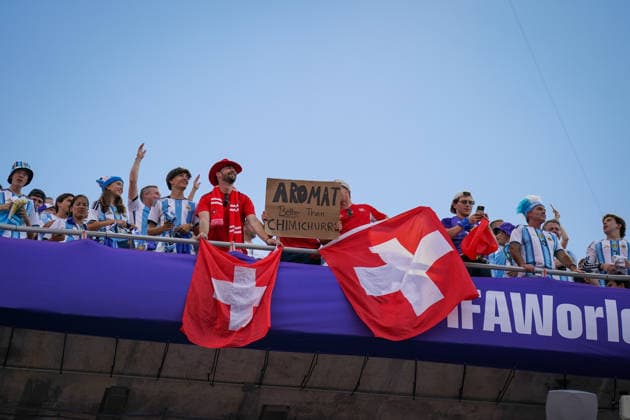 USA: Fussball FIFA World Cup, WM, Weltmeisterschaft, Fussball 2026, Viertelfinale - Argentinien vs Schweiz - Kansas City Stadium (GEHA Field at Arrowhead Stadium, Kansas City, Missouri): Totale der Tribüne mit Schweizer und argentinischen Fußballfans beim Viertelfinale der FIFA Fußball-Weltmeisterschaft 2026. Zwei Schweizer Fahnen hängen am Geländer, ein Fan präsentiert ein humorvolles Plakat mit der Aufschrift Aromat Better Than Chimichurri. Fankultur, Zuschauer, Tribüne, Schweiz, Argentinien, Fahnen, Transparent, Spruchband, Fanblock, Stimmung, WM 2026. *** USA Soccer 2026 FIFA World Cup, Quarterfinal: Argentina vs. Switzerland, Kansas City Stadium (GEHA Field at Arrowhead Stadium), Kansas City, Missouri. A wide shot of the stands filled with Swiss and Argentine soccer fans during the quarterfinal of the 2026 FIFA World Cup. Two Swiss flags hang from the railing, and one fan holds up a humorous sign reading Aromat Better Than Chimichurri. Fan culture, spectators, stands, Switzerland, Argentina, flags, banner, slogan, fan section, atmosphere, 2026 World Cup Copyright: xJOERANxSTEINSIEKx