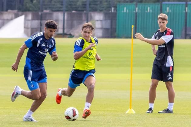Zwei Hamburger SV-Spieler liefern sich einen intensiven Zweikampf um den Ball beim Training, während ein dritter Spieler die Übung beobachtet. Im Hintergrund ist eine gelbe Trainingsstange aufgestellt. Zweikampf im HSV-Training am Volksparkstadion Hamburg *** Two Hamburger SV players are engaged in an intense battle for the ball during practice, while a third player watches the drill. A yellow training cone is set up in the background. Battle for the ball during HSV practice at the Volksparkstadion in Hamburg Copyright: xspeedshotx xAndreasxTolksdorfx