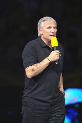 Nikolaj Jacobsen steht mit einem gelben Mikrofon in der Hand vor dunklem Hallenhintergrund und spricht ins Publikum. Auf seinem Unterarm sind mehrere Tattoos sichtbar, darunter Sterne und olympische Ringe. Nikolaj Jacobsen spricht mit Mikrofon in der SAP Arena *** Nikolaj Jacobsen stands in front of a dark arena backdrop, holding a yellow microphone, and speaks to the audience. Several tattoos are visible on his forearm, including stars and the Olympic rings. Nikolaj Jacobsen speaks into the microphone at the SAP Arena. Copyright: xspeedshotx xLukasxTrunkx