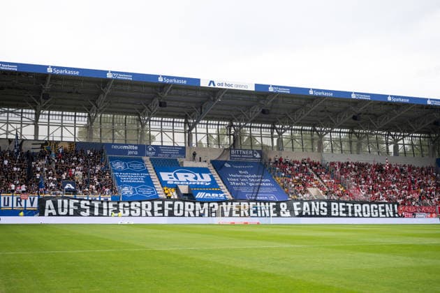 Regionalliga Nordost 2026 27, 1. Spieltag am 26.07.2026 FC Carl Zeiss Jena vs FSV Zwickau Jena und Zwickau Fans mit einem Banner gegen die erneut geplatzte Aufstiegsreform Regionalliga 3. Liga ad hoc Arena im Ernst-Abbe *** Northeast Regional League 2026–27, Matchday 1 on July 26, 2026: FC Carl Zeiss Jena vs. FSV Zwickau; Jena and Zwickau fans display a banner protesting the yet another failed promotion reform for the Regionalliga and 3. Liga, at the ad hoc arena at Ernst Abbe Sport