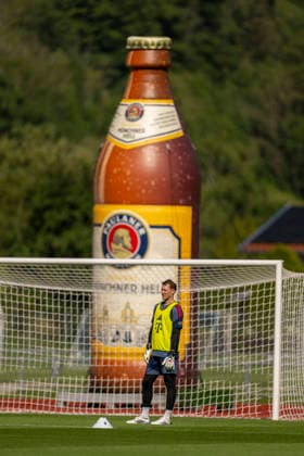 28.07.2026, Fussball Bundesliga 2026 2027, Trainingslager FC Bayern München in Rottach-Egern am Tegernsee (Bayern). Torwart Manuel Neuer (FC Bayern München) steht einsam im Tor, dahinter eine überdimensionale Paulaner Münchner Hell Bierflasche *** July 28, 2026, 2026–2027 Bundesliga, FC Bayern Munich training camp in Rottach-Egern on Lake Tegernsee; Bayern goalkeeper Manuel Neuer stands alone in goal, with an oversized bottle of Paulaner Münchner Hell beer behind him