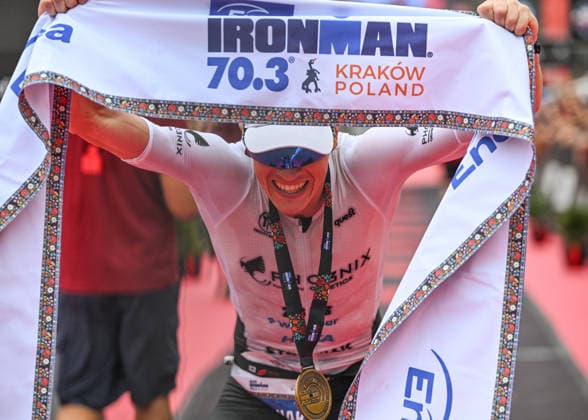 TRIATHLON: Stepniak And Bartlett Secure Elite Victories At IRONMAN 70.3 Krakow KRAKOW, POLAND - AUGUST 02: Professional triathlete Kacper Stepniak of Poland holds the official finish line banner over his head and smiles while wearing his winner s medal after winning the Enea IRONMAN 70.3 Krakow triathlon on the Main Market Square in Krakow, Lesser Poland Voivodeship, Poland, on August 02, 2026. Stepniak successfully defended his championship title, securing first place in the elite professional division with an official time of 3:36:37 following a 113-kilometer (70.3-mile) endurance race across the region. Krakow Poland  Copyright: xArturxWidakx originalFilename:widak-triathlo260802_nppV0.jpg