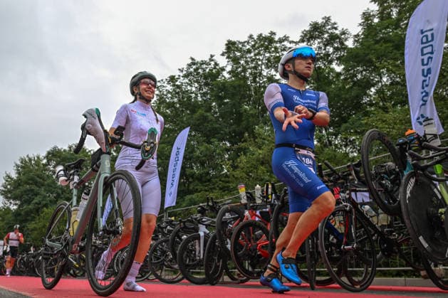 TRIATHLON: Stepniak And Bartlett Secure Elite Victories At IRONMAN 70.3 Krakow KRAKOW, POLAND - AUGUST 02: Triathlete representing the Hampstead Triathlon Club stretches his arms and back while running onto the red carpet alongside another competitor wheeling her Scott road bike inside the Transition 1 (T1) zone during the Enea IRONMAN 70.3 Krakow triathlon in Krakow, Lesser Poland Voivodeship, Poland, on August 02, 2026. Following the opening 1.9-kilometer open-water swim phase inside the Zakrzowek Reservoir, over 2,100 registered competitors rushed to the bike racks to begin the 90-kilometer cycling segment. Krakow Poland  Copyright: xArturxWidakx originalFilename:widak-triathlo260802_npRVt.jpg