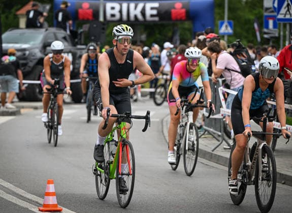 TRIATHLON: Stepniak And Bartlett Secure Elite Victories At IRONMAN 70.3 Krakow KRAKOW, POLAND - AUGUST 02: Triathletes adjust their gear while riding their bicycles out of the Transition 1 (T1) exit gate under an inflatable arch marked BIKE during the Enea IRONMAN 70.3 Krakow triathlon in Krakow, Lesser Poland Voivodeship, Poland, on August 02, 2026. Following the opening swim phase, over 2,100 registered competitors mounted their bicycles to embark on the 90-kilometer (56-mile) bike leg, navigating a high-speed route through the scenic Lesser Poland countryside. Krakow Poland  Copyright: xArturxWidakx originalFilename:widak-triathlo260802_np5OH.jpg