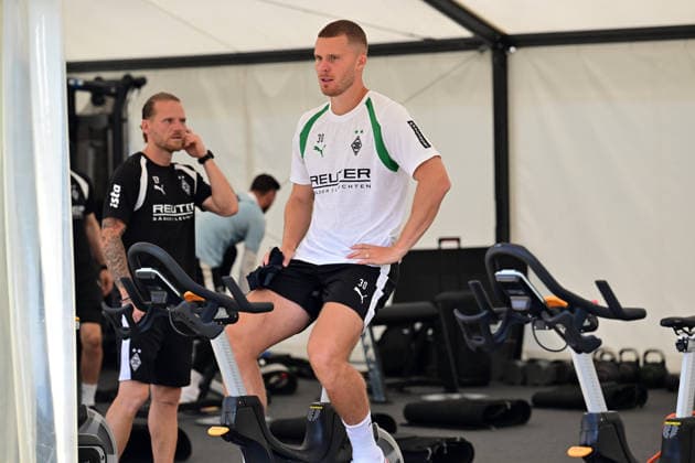 03.08.2026; Rottach-Egern; Fussball, Herren, Saison 2026 2027, Trainingslager Borussia Moenchengladbach Nico Elvedi (Gladbach) auf dem Trainingsrad; im Hintergrund links Eugen Polanski (Trainer Gladbach) DFL regulations prohibit any use of photographs as image sequences and or quasi-video. Stadion Am Birkenmoos Bayern Deutschland *** August 3, 2026 Rottach Egern Soccer, Men s, 2026–2027 season, Borussia Mönchengladbach training camp; Nico Elvedi (Gladbach) on a stationary bike in the background on the left; Eugen Polanski, Gladbach coach; DFL regulations prohibit any use of photographs as image sequences and or quasi-video; Am Birkenmoos Stadium, Bavaria, Germany