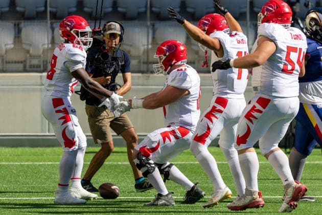 Firenze Red Lions players celebrate on the field during play against the Alpine Rams. Dickson Iwuagwu ( 11) raises both hands in celebration alongside Brandon Belgrave ( 28) and Nelson Diaz Lauzurica ( 58) near a football on the turf. A broadcast camera operator films the play from the background in an outdoor stadium.. Alpine Rams vs Firenze Red Lions, American Football, American Football League Europe, Week 12, 2026, 8.8.2026, Copyright: xPFA RicoxDoninellix