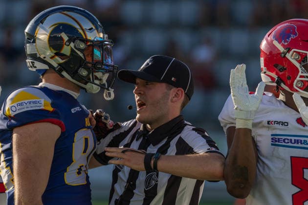 A referee separates an Alpine Rams Fabio Häfliger ( 84) and a Firenze Red Lions player during a stoppage in play. The official extends his arms to de-escalate tension between the opposing players on the field. Both players face each other while the official communicates directly with them. Blurred stadium seating fills the background. Alpine Rams vs Firenze Red Lions, American Football, American Football League Europe, Week 12, 2026, 8.8.2026, Copyright: xPFA RicoxDoninellix