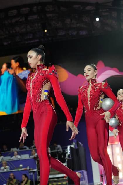 Drei Turnerinnen der ukrainischen Gruppenmannschaft in roten Wettkampfanzügen führen ihre Übung in der Festhalle Frankfurt aus, zwei von ihnen halten silberne Bälle. Im Hintergrund sind weitere Athletinnen und das bunte WM-Dekor sichtbar. Ukraine-Gruppe bei der Gruppenübung – WM Rhythmische Sportgymnastik Frankfurt 2026 *** Three gymnasts from the Ukrainian group team, wearing red competition leotards, perform their routine at the Festhalle in Frankfurt; two of them are holding silver balls. In the background, other athletes and the colorful World Championships decorations are visible. The Ukrainian group during their group routine – 2026 Rhythmic Gymnastics World Championships in Frankfurt Copyright: xspeedshotx