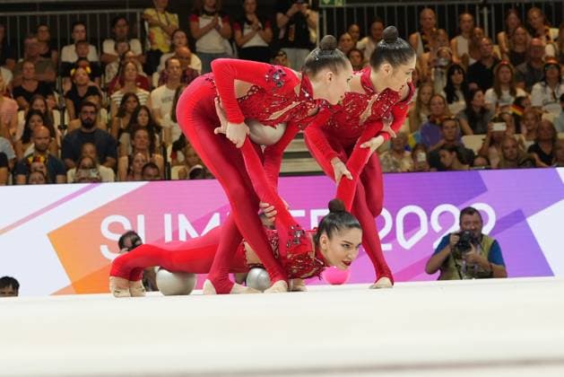 Fünf Turnerinnen in roten Leotards führen eine synchronisierte Gruppenübung mit Bällen in der Festhalle Frankfurt durch. Eine Turnerin liegt am Boden, während ihre Teamkolleginnen sich über sie beugen und die silbernen und rosafarbenen Bälle kontrollieren. Gruppengymnastik-Team bei synchroner Ball-Übung bei der WM 2026 *** Five gymnasts in red leotards are performing a synchronized group routine with balls in Frankfurt’s Festhalle. One gymnast is lying on the floor, while her teammates lean over her and control the silver and pink balls. Group gymnastics team performing a synchronized ball routine at the 2026 World Championships Copyright: xspeedshotx