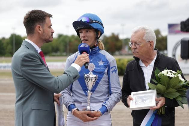 Hannah Schmitz steht nach ihrem Sieg im Rennfahrer-Dress mit blauem Helm und Siegerpokal beim Interview, ein Moderator hält ihr ein Mikrofon hin. Rechts neben ihr überreicht ein älterer Herr Blumen und ein gerahmtes Foto. Hannah Schmitz mit Siegerpokal beim Interview auf der Rennbahn Berlin Mariendorf *** After her victory, Hannah Schmitz stands for an interview in her racing suit, wearing a blue helmet and holding the winner s trophy; a host holds a microphone out to her. To her right, an elderly gentleman presents her with flowers and a framed photo. Hannah Schmitz with the winner s trophy during an interview at the Berlin Mariendorf Racetrack Copyright: xspeedshotx