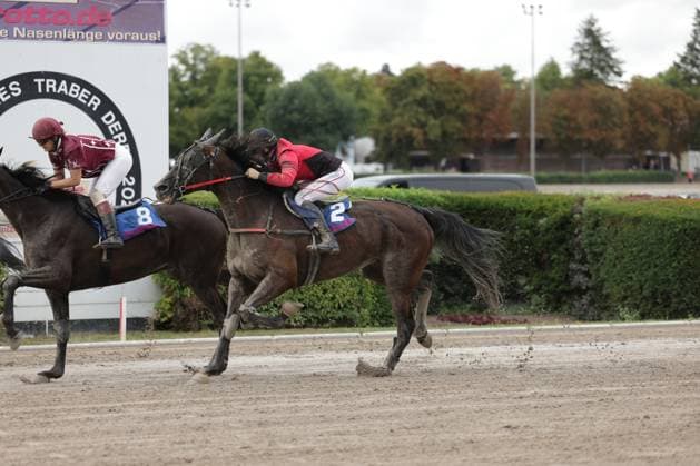 Zwei Jockeys liefern sich auf der Sandbahn in Mariendorf ein enges Duell, Pferd Nummer 2 liegt knapp vor Nummer 8. Der Jockey in Rot-Schwarz liegt tief über dem Hals seines Pferdes, Dreck spritzt unter den Hufen auf. Galopprennen auf der Rennbahn Berlin Mariendorf – Startnummer 2 führt *** Two jockeys are locked in a close battle on the dirt track in Mariendorf; horse number 2 is just ahead of number 8. The jockey in red and black is leaning low over his horse’s neck, and dirt is flying up from under the hooves during the horse race at the Berlin Mariendorf Racetrack—horse number 2 is in the lead. Copyright: xspeedshotx