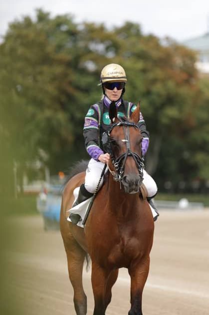 Eine Jockeyfahrerin reitet auf einem braunen Vollblut über die Sandbahn der Rennbahn Berlin Mariendorf. Sie trägt einen goldenen Helm mit der Aufschrift Champion sowie eine dunkel-lila Rennsilk. Jockey auf braunem Vollblut auf der Rennbahn Berlin Mariendorf *** A female jockey rides a bay Thoroughbred across the sand track at the Berlin Mariendorf Racetrack. She is wearing a gold helmet emblazoned with the word Champion and a dark purple racing silks. Female jockey on a bay Thoroughbred at the Berlin Mariendorf Racetrack Copyright: xspeedshotx