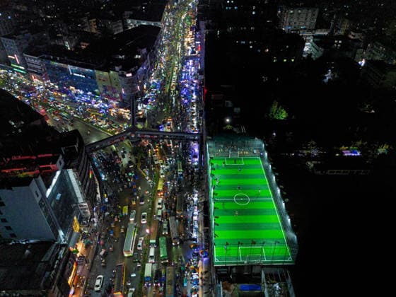 Rooftop Football In A Crowded Megacity People play football on an artificial rooftop field atop an 11-story building in Dhaka, Bangladesh, on August 18, 2026. The field is surrounded by dense buildings, busy streets and heavy traffic. Dhaka Bangladesh  Copyright: xBipulxAhmedx originalFilename:mondol-notitle260818_npy7r.jpg