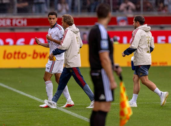 18.08.2026, Fussball Bundesliga 2026 2027, Testspiel, 1.FC Heidenheim - FC Bayern München, in der Voith-Arena Heidenheim, nach seinem erneuten Zusammenbruch während des Spieles, wird Jamal Musiala (li, Bayern München) vom Mannschaftsarzt Prof. Dr. Peter Ueblacker versorgt und vom Platz geführt. *** August 18, 2026, 2026–2027 Bundesliga season, friendly match, 1. FC Heidenheim vs. FC Bayern Munich, at the Voith Arena in Heidenheim; after collapsing again during the game, Jamal Musiala (left), of Bayern Munich, is treated by team doctor Prof. Dr. Peter Ueblacker and led off the field