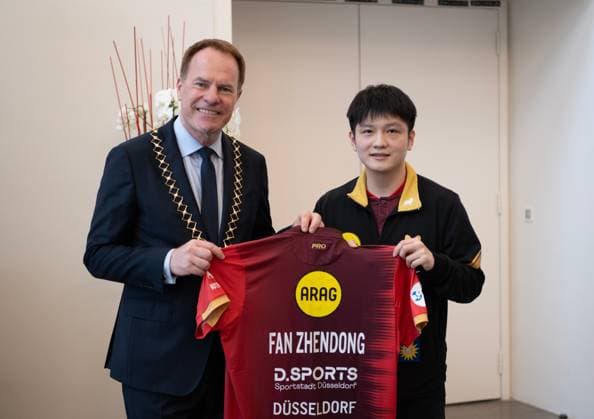 (260821) -- BEIJING, Aug. 21, 2026 -- Fan Zhendong (R) gives his jersey to Stephan Keller, mayor of Dusseldorf, during the welcoming ceremony in Dusseldorf, Germany, Aug. 20, 2026. Chinese Table tennis, Tischtennis star Fan Zhendong was officially unveiled by his new club Borussia Dusseldorf at a press conference, PK, Pressekonferenz here on Thursday, as the Olympic champion prepares for his second season in the German Table Tennis Bundesliga and another campaign in European competition. ) XINHUA PHOTOS OF THE DAY ZhangxHaofu 
