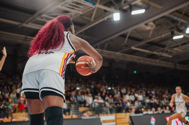 Eine Spielerin der deutschen Damen-Nationalmannschaft hält den Basketball und bereitet einen Pass oder Wurf vor, aufgenommen aus einer tiefen Froschperspektive hinter dem Rücken der Spielerin. Im Hintergrund ist eine weitere deutsche Spielerin in Bewegung sowie eine gut gefüllte Tribüne zu sehen. Deutschland A-Natio Damen mit Ball in der Sparkassen-Arena Göttingen *** A player on the German women s national team is holding the basketball and preparing to pass or shoot, shot from a low, low-angle perspective behind the player s back. In the background, another German player can be seen in motion, as well as a packed stands. Germany Women s National Team with the ball at the Sparkassen Arena in Göttingen Copyright: xJoelxKruehlerx