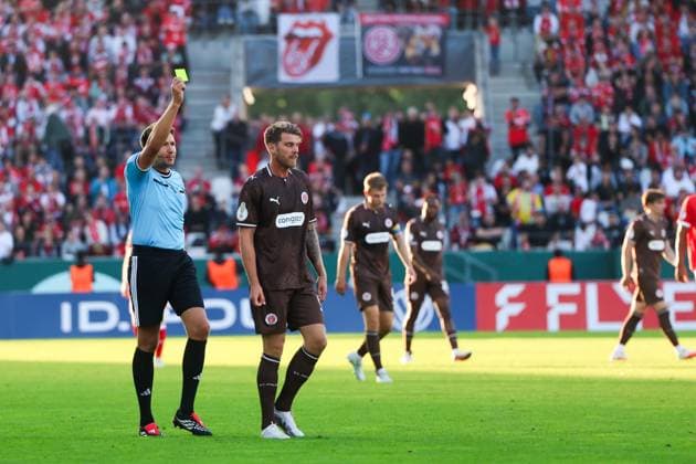 Schiedsrichter zeigt Marcus Mathisen von FC St. Pauli die Gelbe Karte im Spiel gegen Rot-Weiss Essen im Stadion an der Hafenstraße. Weitere St.-Pauli-Spieler sind im Hintergrund zu sehen, die Tribünen sind mit rot-weißen Essen-Fans gefüllt. Marcus Mathisen (FC St. Pauli) sieht Gelbe Karte im DFB-Pokal *** The referee shows Marcus Mathisen of FC St. Pauli a yellow card during the match against Rot-Weiss Essen at the Stadion an der Hafenstraße. Other St. Pauli players can be seen in the background, and the stands are filled with red-and-white Essen fans. Marcus Mathisen of FC St. Pauli receives a yellow card in the DFB Cup. Copyright: xRuhr.Pottraitx