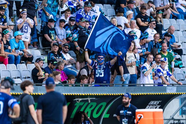A Nordic Storm fan with blue face paint waves a large team flag while cheering. 29.08.2026, Innsbruck, European Football Alliance, Championship Game, Munich Ravens - Nordic Storm. Innsbruck Tivoli Stadium Austria Copyright: xPFA RicoxDoninellix