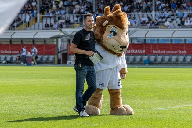 Sebastian Schaech, stadium announcer for TSV 1860 Munich, and Sechzgerl, the TSV 1860 Munich mascot, on the field in front of the GER fan section during the TSV 1860 Munich vs. TSV Landsberg 1882 match, Soccer, Bavarian Regional League, Matchday 6, 2026–2027 season, August 30, 2026. DFL and DFB regulations prohibit any use of photographs as image sequences and or quasi-video. Photo: HMB Media, Heike Feiner Copyright: HMBxMedia HeikexFeiner