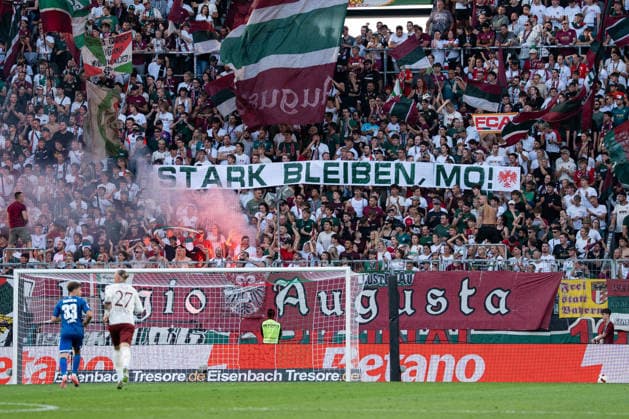 Fussball: Deutschland: 1. Bundesliga 2026 2027 - 1. Spieltag, 30.08.2026 - FC Augsburg vs. FC Schalke 04 (WWK Arena, Augsburg); Banner, Fankurve FC Augsburg, Fans, Stark bleiben, Mo! *** Soccer Germany 1 Bundesliga 2026–2027 Matchday 1, August 30, 2026 FC Augsburg vs. FC Schalke 04 WWK Arena, Augsburg Banner, FC Augsburg Fan Section, Fans, Stay Strong, Mon Copyright: xValentinxDomgjonix