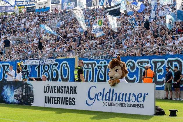 TSV 1860 Munich’s mascot, Sechzgerl, behind a Loewenstark advertising banner; Geldhauser die Muenchner Busreisen on the road, with the Westkurve stand and the Loewenfans GER behind it, TSV 1860 Munich vs. TSV Landsberg 1882, soccer, Bavarian Regional League, Matchday 6, 2026–2027 season, August 30, 2026. DFL and DFB regulations prohibit any use of photographs as image sequences and or quasi-video. Photo: HMB Media, Heike Feiner Copyright: HMBxMedia HeikexFeiner