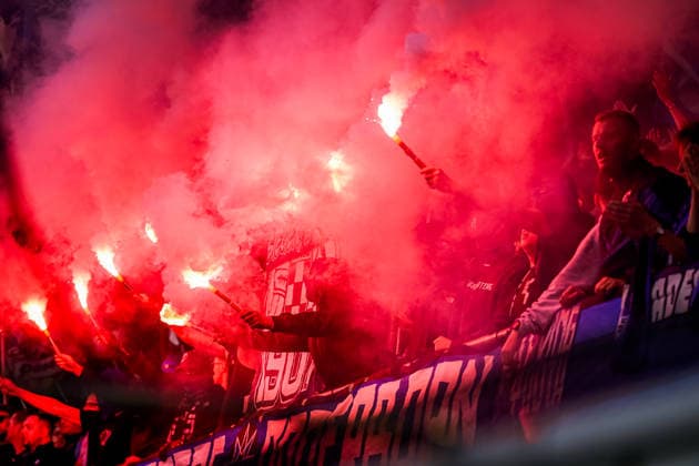 Deutschland: Fussball Bundesliga 2026 - 2027, 2. Spieltag - SC Paderborn 07 vs SC Freiburg - Home-Deluxe-Arena (Paderborn): Zuschauer, Fans auf der Tribüne mit brennender roter Pyrotechnik und Bengalos. Dichter roter Rauch über dem Fanblock, mehrere Fans halten Leuchtfackeln in den Händen. Fahnen und Transparente im Zuschauerbereich. *** Germany Soccer Bundesliga 2026–2027, Matchday 2: SC Paderborn 07 vs. SC Freiburg at the Home Deluxe Arena in Paderborn; spectators and fans in the stands with burning red pyrotechnics and flares; thick red smoke over the fan section; several fans holding torches; flags and banners in the spectator area Copyright: xJOERANxSTEINSIEKx