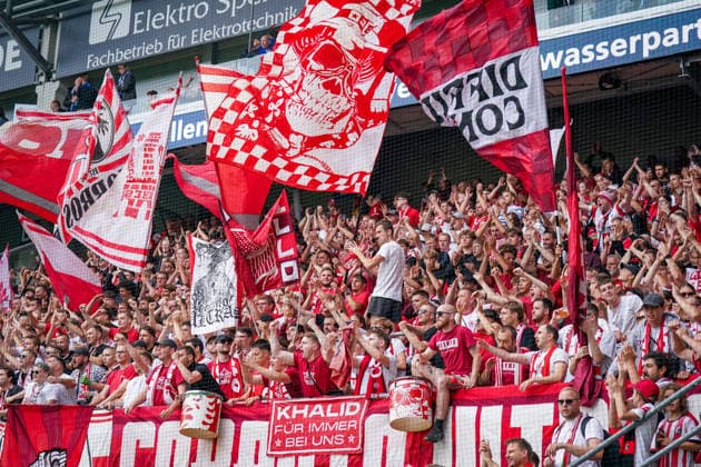 Deutschland: Fussball Bundesliga 2026 - 2027, 2. Spieltag - SC Paderborn 07 vs SC Freiburg - Home-Deluxe-Arena (Paderborn): Zuschauer, Fans des SC Freiburg auf der Tribüne, Fanblock mit zahlreichen rot-weißen Fahnen und Schals. Fans klatschen und feuern ihre Mannschaft an. Mehrere Trommeln sowie Transparente und Spruchbänder sind im dicht besetzten Gästeblock zu sehen. *** Germany Soccer Bundesliga 2026–2027, Matchday 2: SC Paderborn 07 vs. SC Freiburg at Home Deluxe Arena Paderborn; spectators, SC Freiburg fans in the stands, a fan section with numerous red-and-white flags and scarves; fans clapping and cheering on their team; several drums, as well as banners and signs, can be seen in the packed visitors’ section Copyright: xJOERANxSTEINSIEKx
