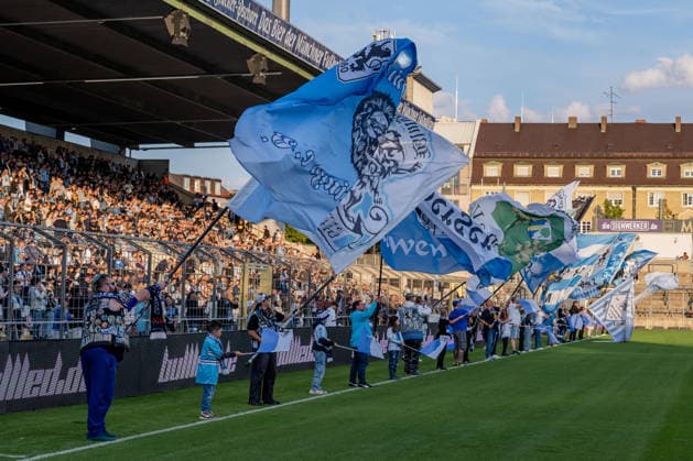 The flag-wavers in front of the standing-room-only section before the start of the match between GER, TSV 1860 Munich, and TSV Schwaben Augsburg, soccer, Bavarian Regional League, Matchday 8, 2026–2027 season, September 11, 2026 DFL DFB REGULATIONS PROHIBIT ANY USE OF PHOTOGRAPHS as IMAGE SEQUENCES and or QUASI-VIDEO Photo: HMB Media, Heike Feiner Copyright: HMBxMedia HeikexFeiner