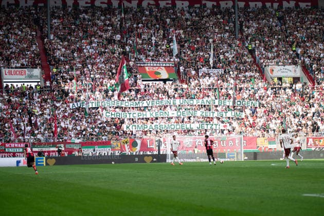 FC Augsburg Fans mit dem Banner Aufstiegsreform? Vereine uns Fans betrogen! Chrisoph Kern- Deine Zeit ist um! Kompassmodell jetzt! beim Bundesligaspiel FC Augsburg - Bayer 04 Leverkusen am 12.09.2026. Augsburg WWK Arena Bayern Deutschland *** FC Augsburg fans holding a banner reading: Promotion Reform: Clubs and Fans Have Been Betrayed Christoph Kern, Your Time Is Up Compass Model at the Bundesliga match between FC Augsburg and Bayer 04 Leverkusen on September 12, 2026, at the WWK Arena in Augsburg, Bavaria, Germany