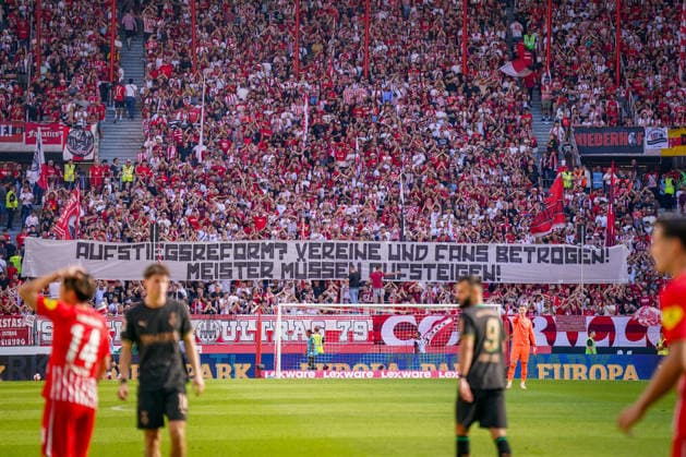 Deutschland: Fussball Bundesliga 2026 - 2027, 3. Spieltag - SC Freiburg vs Borussia Mönchengladbach - Europa-Park-Stadion (Freiburg): Fans des SC Freiburg auf voll besetzter Tribüne mit großem Spruchband Aufstieg reform? Vereine und Fans betrogen! Meister müssen aufsteigen!. Fanprotest, Aufstiegsreform, Regionalliga, Aufstiegsregelung, DFB, Fußball, Fans, Ultras, Zuschauer, Fankurve, Transparent, Spruchband, Protestbanner, Stadion, SC Freiburg. *** Germany Soccer Bundesliga 2026–2027, Matchday 3: SC Freiburg vs. Borussia Mönchengladbach at Europa-Park Stadium in Freiburg. SC Freiburg fans in a packed stands holding a large banner reading: Promotion Reform—Clubs and Fans Betrayed—Champions Must Be Promoted. Fan protest, promotion reform, Regionalliga, promotion rules, DFB, soccer, fans, ultras, spectators, fan section, banner, protest banner, stadium, SC Freiburg Copyright: xJOERANxSTEINSIEKx