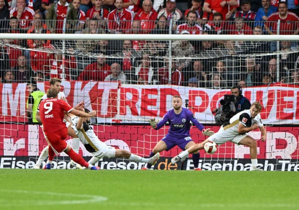 German Bundesliga Season 2026-27, September 13, 2025, Ursapharm Arena, SV Elversberg (ELV) vs. FC Bayern Munich (FCB), 1-2. Harry KANE of FC Bayern Munich (No. 9) takes a shot, Goalkeeper Nicolas KRISTOF (SV Elversberg, center), and Lasse GUENTHER (SV Elversberg) clear the ball for a corner. German Bundesliga SV Elversberg