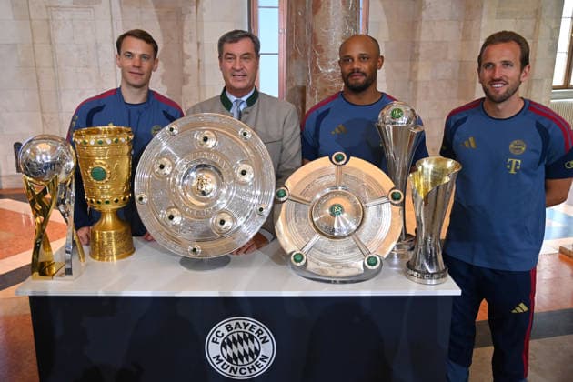 From left: Manuel NEUER, goalkeeper for Bayern Munich; Markus SOEDER, Minister-President of Bavaria and CSU Chairman; Coach Vincent KOMPANY of Bayern Munich; and Harry KANE of Bayern Munich stand behind the trophies, cups, and awards won during the 2025–26 season,Championship Trophy, DFB Cup, and Super Cup. Markus SÖDER, Minister-President of Bavaria and CSU Chairman, welcomes the championship teams of FC Bayern Munich to the Kuppelsaal at the State Chancellery in Munich on September 16, 2026.