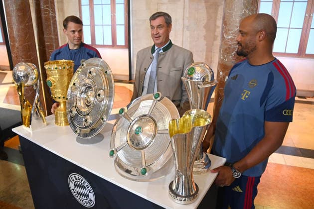 From left: Manuel NEUER, goalkeeper for Bayern Munich; Markus SOEDER, Minister-President of Bavaria and CSU Chairman; and Vincent KOMPANY, coach of Bayern Munich, stand behind the trophies, cups, and awards won during the 2025–26 season:Championship Trophy, DFB Cup, and Super Cup. Markus SÖDER, Minister-President of Bavaria and CSU Chairman, welcomes the championship teams of FC Bayern Munich to the Kuppelsaal at the State Chancellery in Munich on September 16, 2026.
