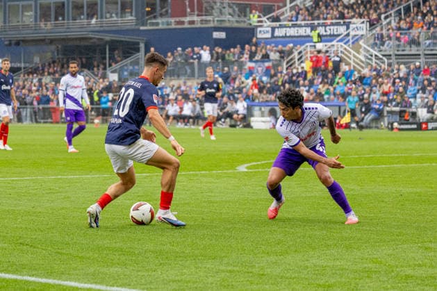 September 19, 2026 Soccer 2. Bundesliga Men s 2026–2027 Season, Matchday 6: Holstein Kiel vs. VFL Osnabrück; Kiel in blue and white, Osnabrück in white and purple; Adrian Kapralik (left), Jonathan Gomez, Holstein Kiel Stadium, Westring 501, Schleswig-Holstein, Germany