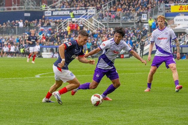September 19, 2026 Soccer 2. Bundesliga Men s 2026–2027 Season, Matchday 6: Holstein Kiel vs. VFL Osnabrück; Kiel in blue and white, Osnabrück in white and purple; Adrian Kapralik (left), Jonathan Gomez, Holstein Kiel Stadium, Westring 501, Schleswig-Holstein, Germany