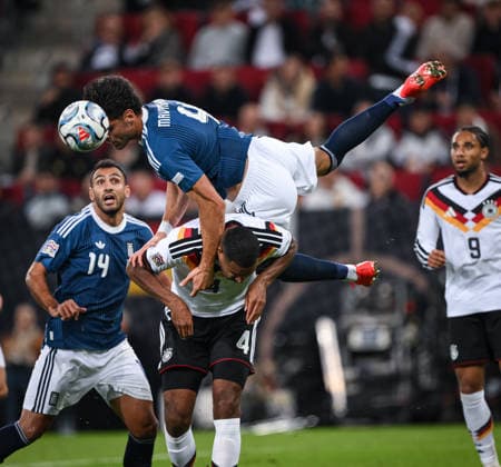 SOCCER UEFA Nations League League A Group 2 2026–2027 in Augsburg, September 27, 2026: Germany vs. Greece. Ntinos Mavropanos (top), Greece, jumps over Jonathan Tah (bottom), Germany, watched by Vangelis Pavlidis (left), Greece.