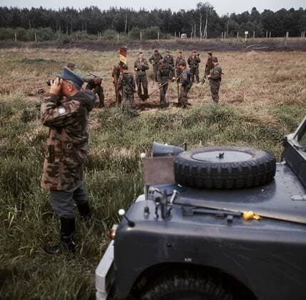 Deutsche Grenze 1978 bei Helmstedt - BRD-Grenzbeamter schaut durch seinen Feldstecher während DDR-Grenzsoldaten einen Grenzpfahl setzen