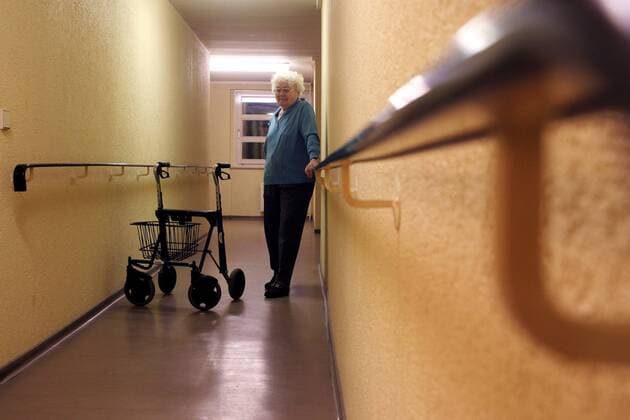 Rentnerin mit Gehhilfe auf dem Flur eines Seniorenheims