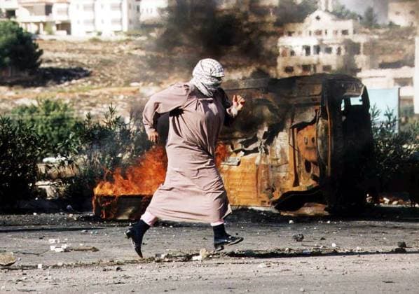 Fliehende Palästinenserin rennt an einem brennenden Autowrack vorüber während eines Straßenkampfes in Ramallah  ram2000102602