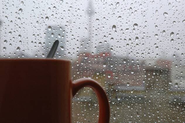 Sauwetter: Tasse Tee mit Löffel vor einer verregneten Fensterscheibe in Berlin
