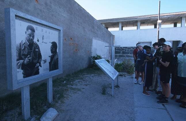 IMAGO History, Ende der Apartheid in Südafrika: 1990-1994 Besucher vor einer Tafel mit einem Foto des inhaftierten Nelson Mandela in der ehemaligen Gefängnisanlage auf Robben Island
