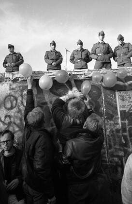 Luftballons schmücken die bereits von Mauerspechten bearbeitete Berliner Mauer unter den Augen von Volksarmisten - Mauerfall in Berlin