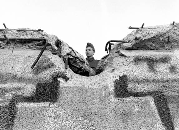 Soldat der Grenztruppen schaut über teilzerstörte Berliner Mauer - iblzni01084378